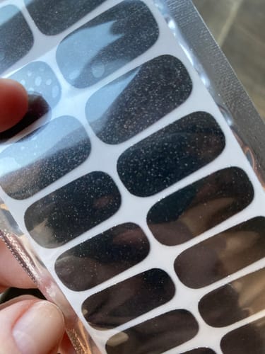 Rezensent hält die schwarzen, glitzernden Midnight Glitter Nagelfolien in der Verpackung.