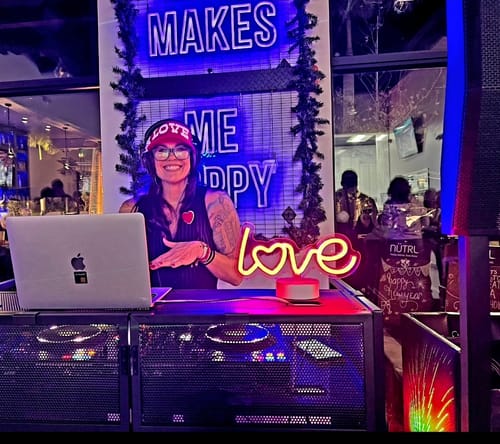 Reviewer smiling at a DJ booth wearing the red Big Love Trucker hat.
