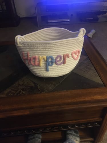 Customer's personalized white knitted basket with "Harper" in multicolor yarn and a pink heart icon.