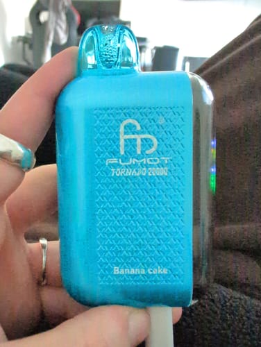 Ein Kunde hält den leuchtblauen RANDM TORNADO 20000 Vape in der Geschmacksrichtung 'Banana Cake' in der Hand.