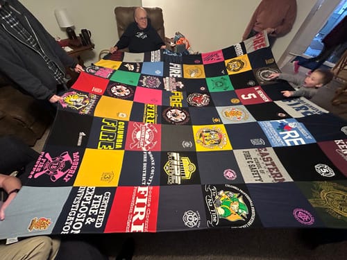 Customer's family holding up a large Premium T Shirt Quilt made from colorful shirts with various logos in their living room.