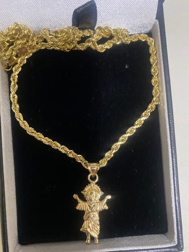 Reviewer's gold Divino Niño pendant and rope chain displayed inside a black jewelry box.