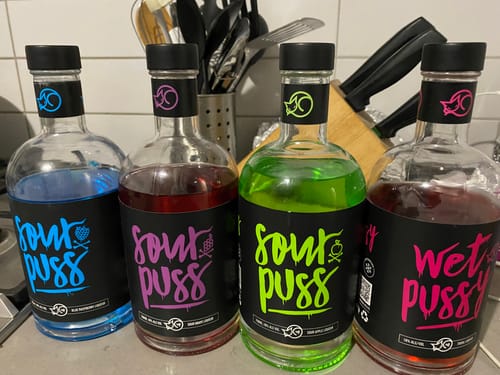 Customer's green Sour Puss Apple liqueur bottle lined up with three other colorful liqueur bottles.