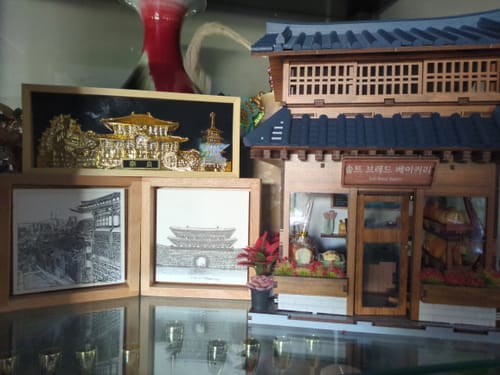 Customer's detailed, assembled Ikseon-dong Hanok Bakery Miniature House Kit on display with other decorative items.