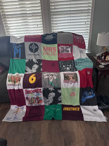 Customer's large, colorful Premium T Shirt Quilt made from various t-shirts, draped over a sofa in a living room.