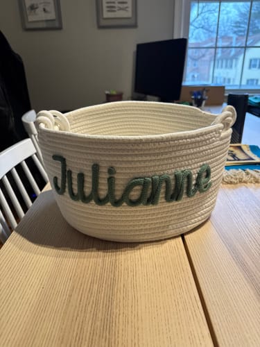 Customer's personalized knitted basket with 'Julianne' embroidered in green, shown on a wooden table.