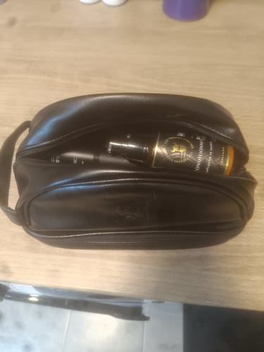 Un client montre la trousse de voyage noire Max-Barber® sur une table, avec un produit de soin à l'intérieur.