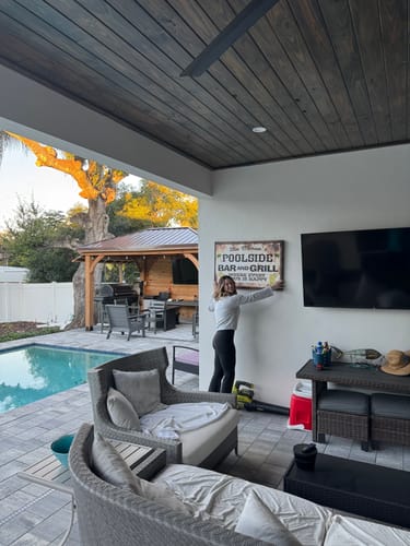 Customer hanging a custom 'Poolside Bar and Grill' sign on an outdoor patio wall next to a pool.