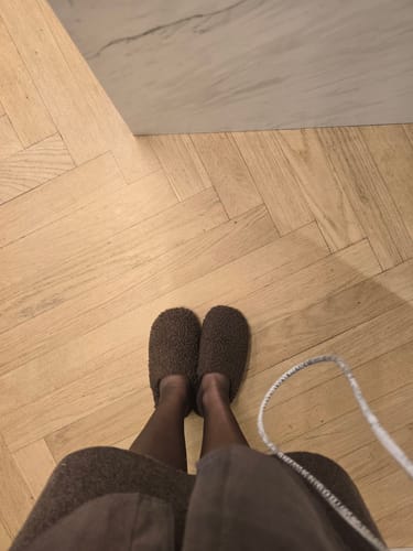 לקוחה נועלת נעלי בית חומות ורכות מדגם Lamb על רצפת עץ.