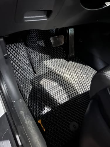 Recenzent pokazuje czarny dywanik samochodowy idealnie dopasowany do podłogi po stronie kierowcy.