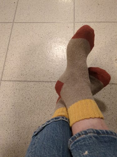 Customer wearing the color-blocked wool socks with jeans. The socks are beige with a yellow cuff and a rust-colored toe.