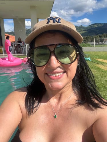 Cliente sorrindo em uma selfie usando os Óculos Veneza grandes perto de uma piscina.