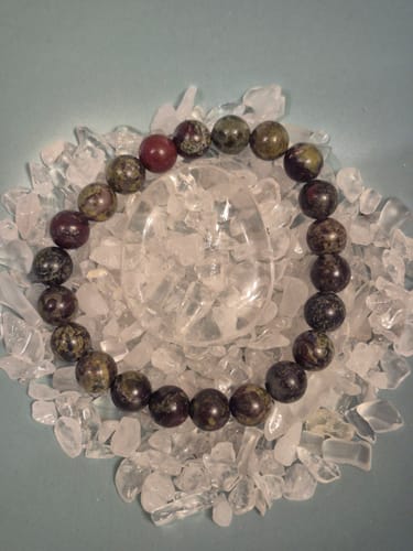 Photo d'avis du bracelet Jaspe Sang de Dragon, avec ses perles vertes et rouges, posé sur des cristaux.