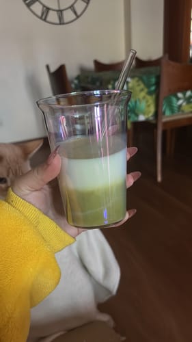 Un cliente sostiene un vaso de cristal con Té Matcha Vainilla Premium preparado en capas.