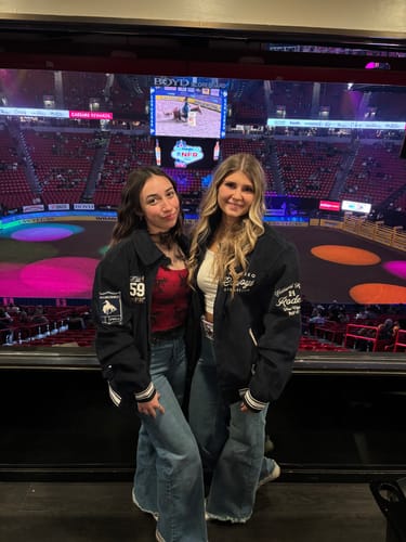 Reviewer and a friend wearing matching navy Vintage NFR Corduroy Bombers at a rodeo arena.