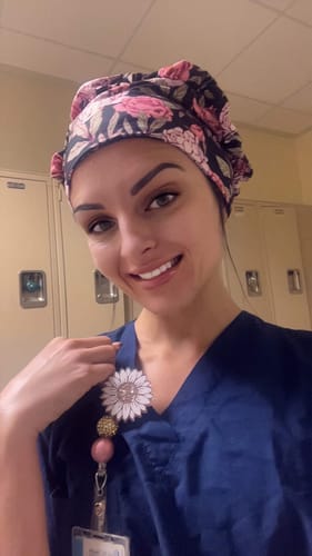 Reviewer smiling in a locker room, wearing the DuoStyle Scrub Hat with a pink peonies pattern.