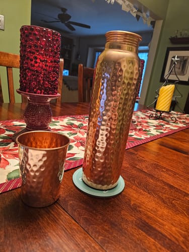 Customer's hand-hammered copper water bottle and matching cup displayed on a wooden dining table.