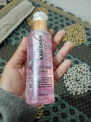 Customer holding the clear pump bottle of LuminaBright Whitening Face Wash, revealing the pink gel cleanser.