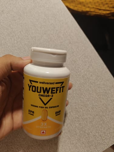 A customer holding the YouWeFit Omega-3 Fish Oil bottle against a textured surface.