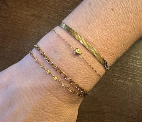 Customer wearing the Essentials Bracelet, a flat gold herringbone chain, stacked with other bracelets.