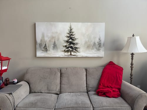 Reviewer's Snowy Christmas Tree wall art hanging in their living room above a grey couch.