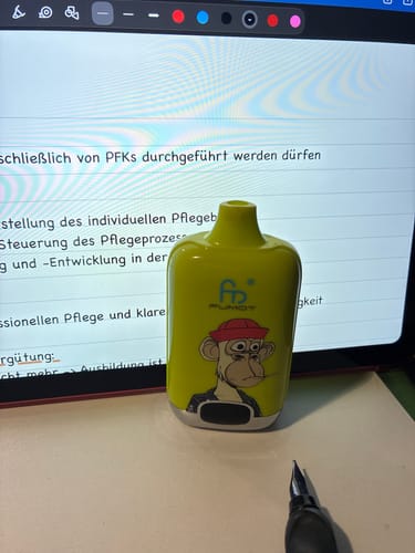 Ein Kunde zeigt seinen leuchtend gelben RANDM Digital Box 12000 Vape mit Affen-Design auf einem Schreibtisch.