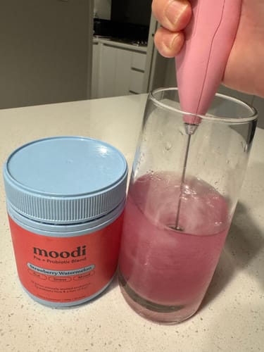 Customer mixing the pink Strawberry Watermelon drink in a glass with an electric frother, with the product container on the side.