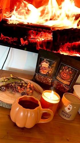 Rezensent zeigt das Kerzen-Set in einer gemütlichen Herbstszene. Eine Kerze brennt neben einer Kürbistasse vor einem Kamin.