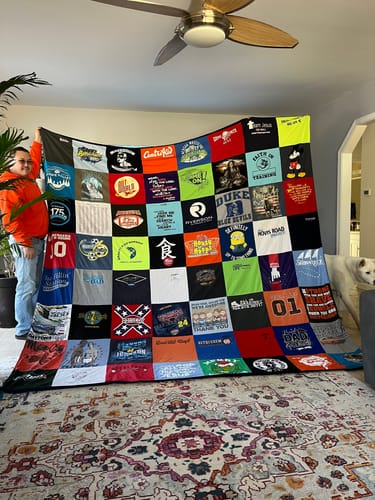 Customer proudly displaying their large Premium T-Shirt Quilt, made from a colorful grid of many different t-shirts.