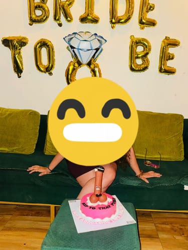 Customer's pink erotica bachelorette cake on a table at a party, with 'BRIDE TO BE' balloons in the background.