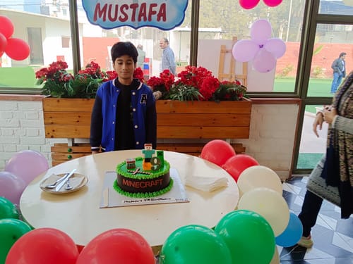 Customer's vibrant Minecraft Game Cake on a party table, with a young boy standing behind it.