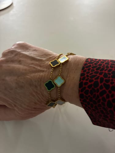 Close-up of a reviewer's wrist wearing two gold-tone bracelets with colorful clover charms.