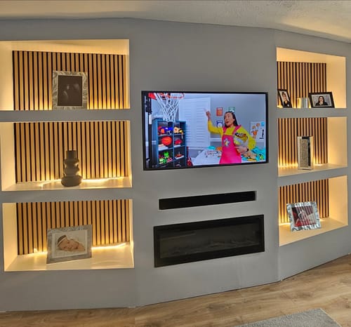 Reviewer's acoustic slatted wall panels installed as a backdrop in illuminated shelves on a media wall.