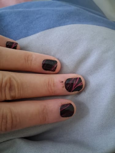 Nahaufnahme der Hand einer Kundin mit den 'Sienna Silk' Nagelfolien in Schwarz mit roten Linien.