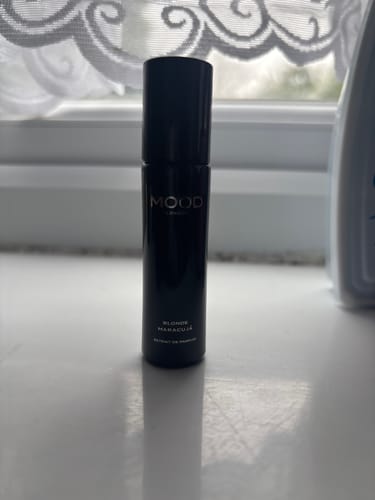 Reviewer's black bottle of Blonde Maracujá fragrance oil standing on a white surface in front of a window.