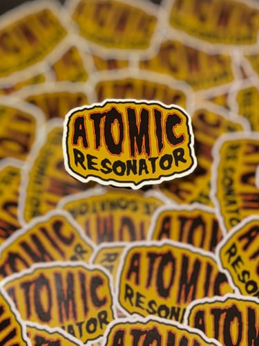 Customer's pile of custom stickers. The top sticker is yellow and black with 'ATOMIC RESONATOR' text.