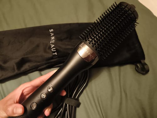 Een recensent houdt de zwarte SANSBEAUTÉ® WET-TO-DRY FÖHNBORSTEL vast met het bijbehorende opbergetui op de achtergrond.