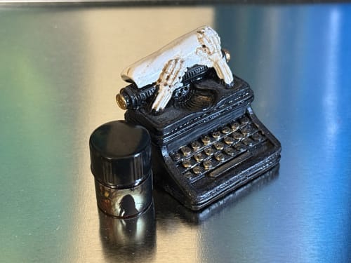 Customer's small bottle of The Morrigan fragrance next to a miniature black typewriter with skeletal hands.