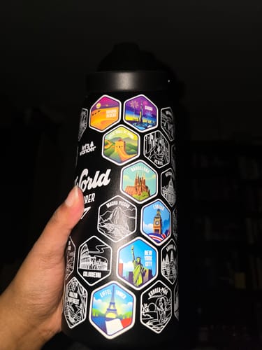 Customer holding their black World Explorer Bottle with several colorful landmark stickers applied over the engravings.
