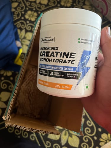 Customer holding a white tub of Wellcore Creatine Monohydrate over the open shipping box.
