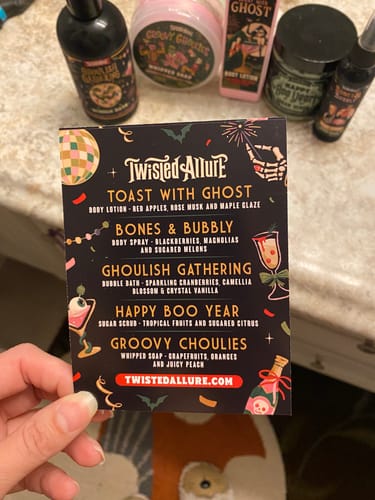 Customer's hand holding a spooky-themed card listing the scents in the Monthly Subscription Box.