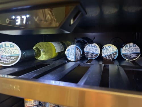 Customer's tins of Classic Nicotine Pouches being kept cool in a wine fridge next to a bottle of wine.