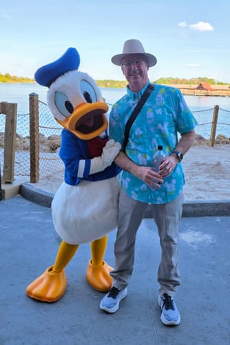 Customer wearing the tropical Disney "Island Smilin'" shirt while posing with the Donald Duck character outdoors.