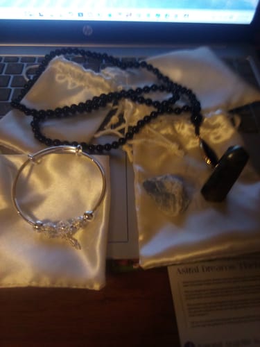 Customer's AuraBloom Subscription Box contents displayed on a desk, including a black necklace, silver bracelet, and crystals.