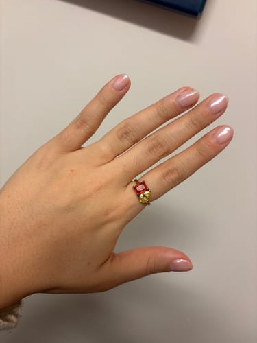 Reviewer's hand wearing the shiny Toi Et Moi Birthstone Ring with a red emerald-cut and a yellow pear-cut stone.
