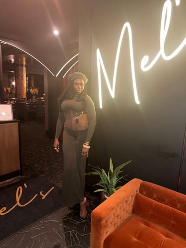 Reviewer standing indoors wearing the full-length, dark NW Sculpt Wide-Leg Jumpsuit, styled with a beret and corset.