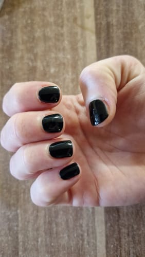 Hand einer Kundin, die ihre glänzend schwarzen Nägel mit den UV-Gelfolien 'Midnight Waltz' zeigt.