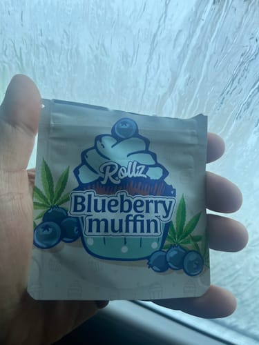 Customer's hand holding the illustrated packaging for Blueberry Muffin THCA Flower inside a car.