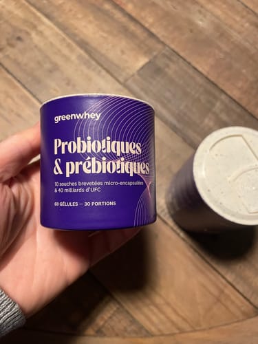 Un client tient le pot en carton violet des Probiotiques & Prébiotiques dans sa main sur un fond en bois.