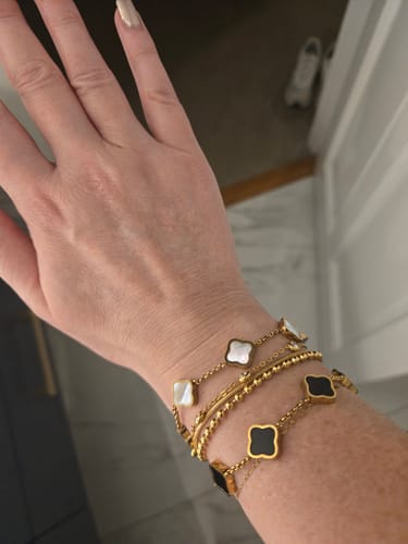 Customer's wrist showing stacked Celine Clover Bracelets in white mother of pearl and black enamel.
